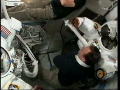 Podgląd na wnętrze przedziału sprzętowego modułu Quest, w którym trwają przygotowania do spaceru kosmicznego. W tle widoczne skafandry EMU, w które niebawem ubierani będą Fincke i Chamitoff / Credits: NASA TV