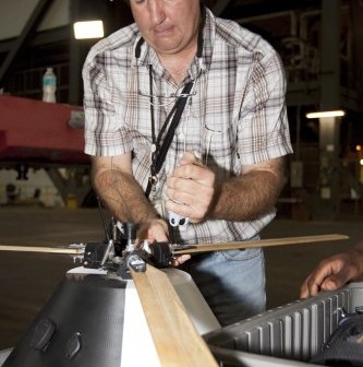 Zdjęcie: Inżynier NASA Jeff Hagen przytwierdza wirnik do górnej części modelu kapsuły tuż przed testami opadania w budynku Vehicle Assembly w Kennedy Space Center. Credit: NASA/Kim Shiflett
