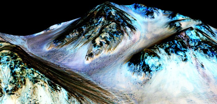 Ciemne, 100-metrowe smugi wskazują na występowanie płynnej wody na Marsie. Naukowcy odkryli uwodnione sole w ciemnych smugach. Niebieskie obszary to minerał piroksen, nie związany bezpośrednio z potokami solanki. Credits: NASA/JPL/University of Arizona