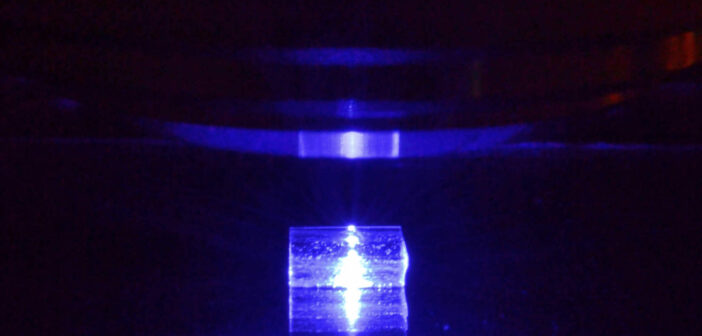 Pobudzany światłem niebieskim kryształ fluorku litu z zarejestrowanymi śladami cząstek jonizujących podczas obserwacji pod mikroskopem fluorescencyjnym. (Źródło: IFJ PAN)